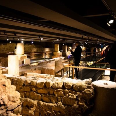 Vista d'una sala amb runes parets i columnes i alguns visitants mirant-les.
