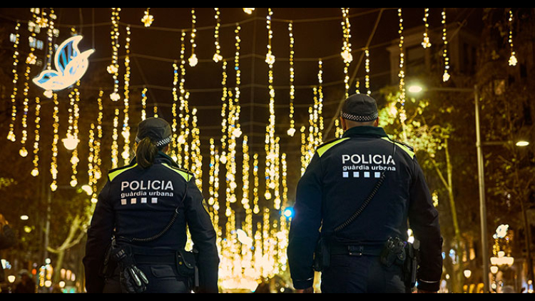 Two Guàrdia Urbana police officers patrolling a street in Barcelona, which is decorated for Christmas.